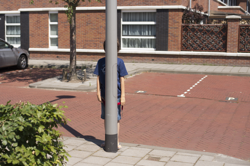 foto van een jongen die zich verstopt achter een lantaarnpaal