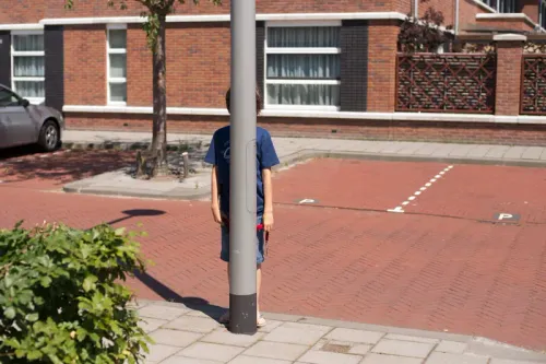 foto van een jongen die zich verstopt achter een lantaarnpaal